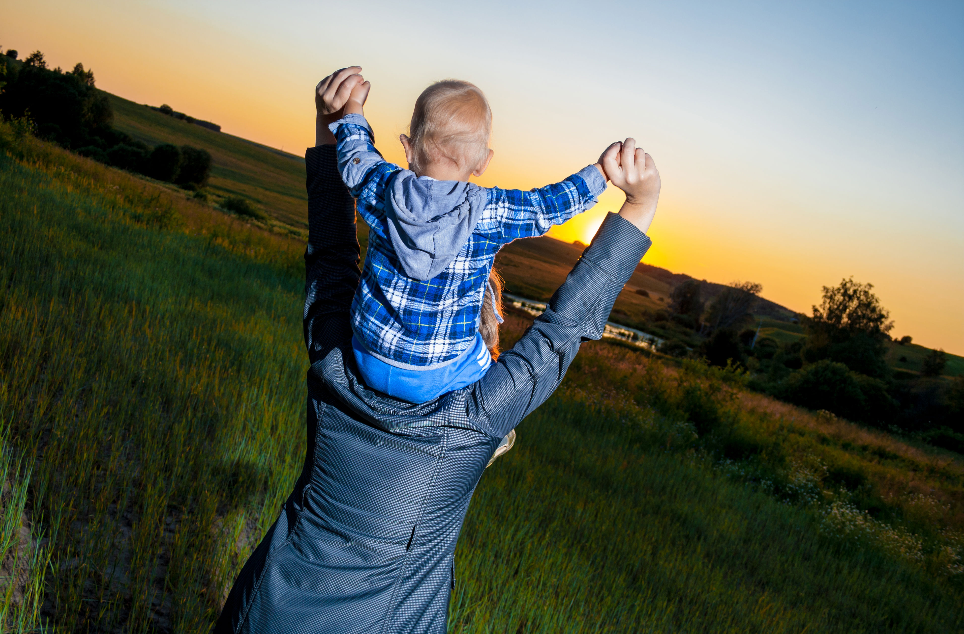 Barn på voksen skulder i solnedgang