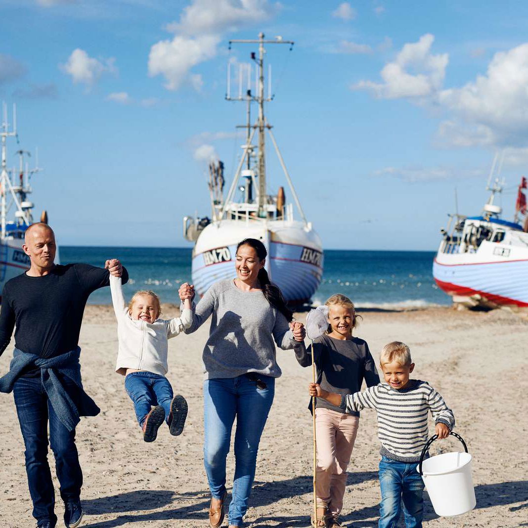 Familie med tre børn på strand med fiskerbåde